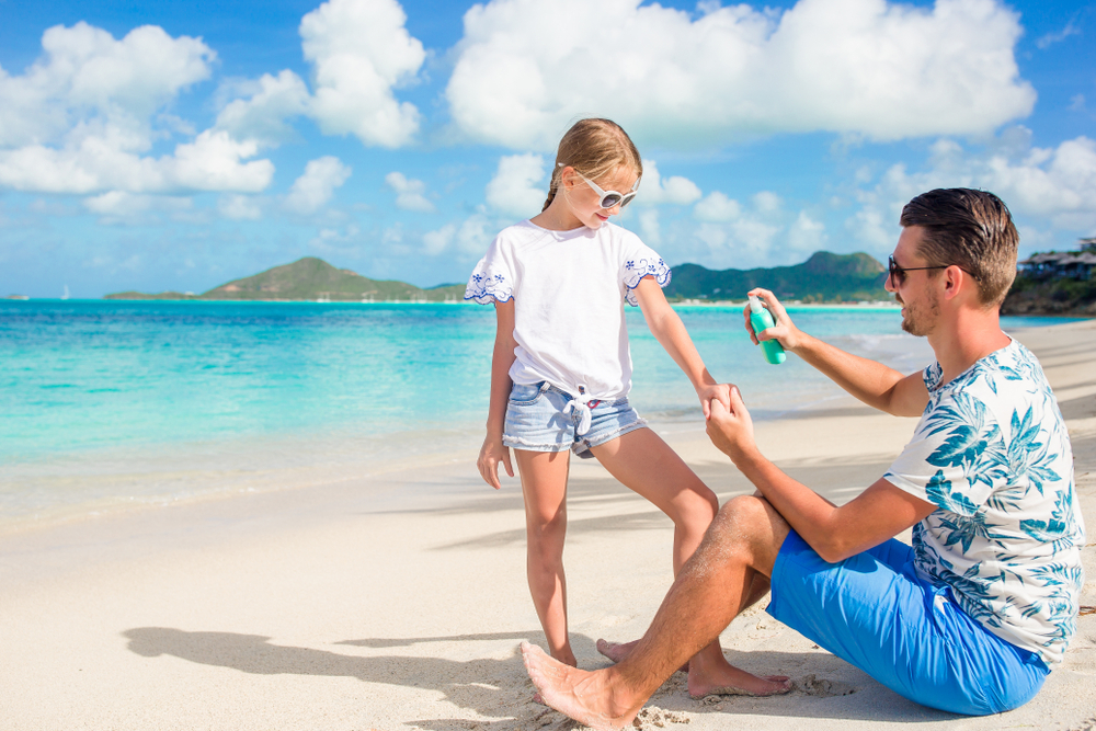 Papà mette la crema solare a sua figlia in spiaggia