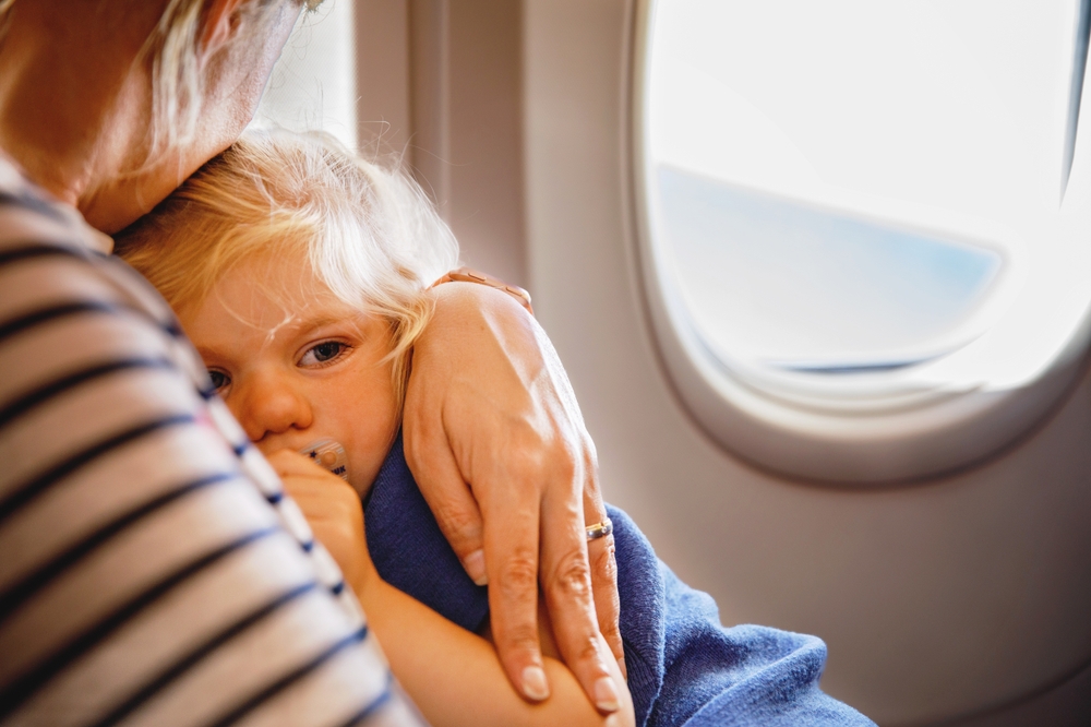Bambina con raffreddore in braccio alla mamma in aereo