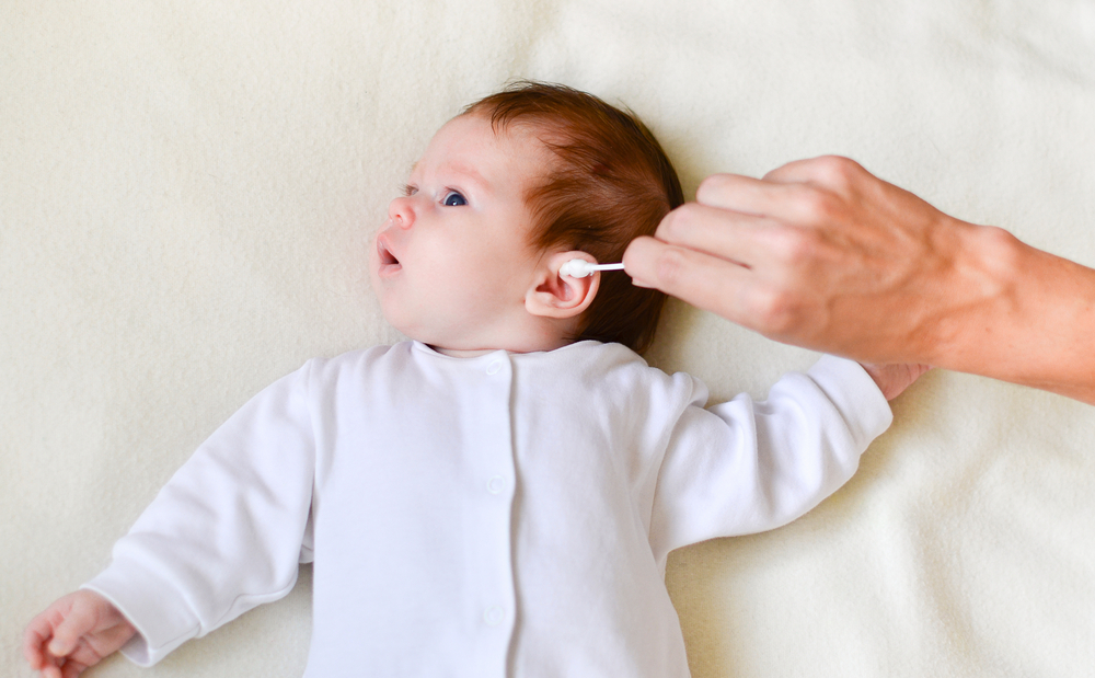 Mano di una mamma che pulisce delicatamente le orecchie del neonato con un cotton fioc morbido