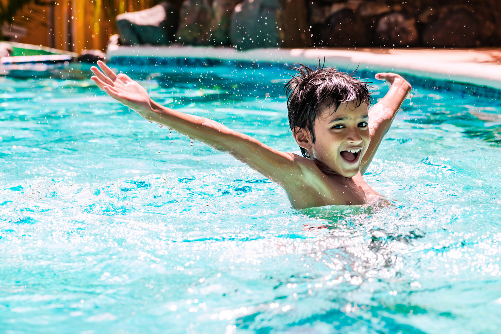 Bambino sorridente all'interno di una piscina con le braccia aperte