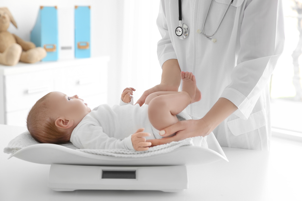 Pediatra che pesa un neonato sulla bilancia elettronica durante una visita di controllo