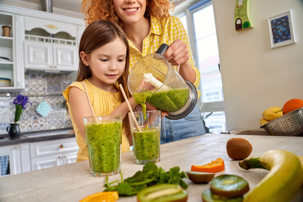 Mamma e figlia in cucina che preparano uno smoothie verde con il frullatore