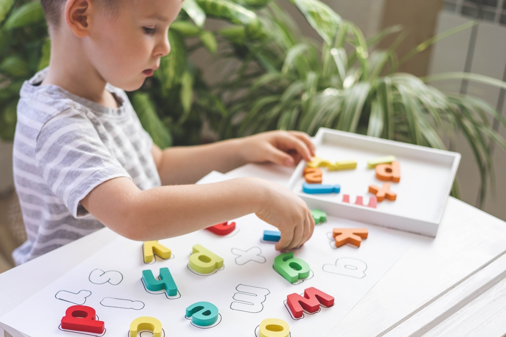 Bambino seduto al tavolo che gioca con le lettere in legno