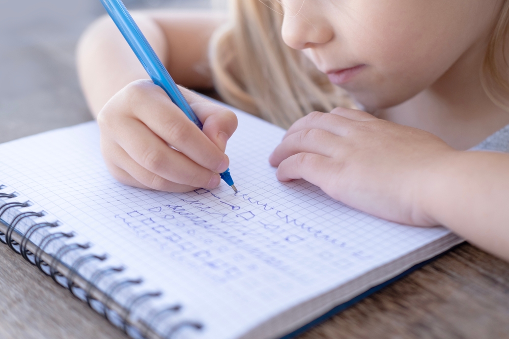 Bambina che scrive con una penna su un quaderno bianco