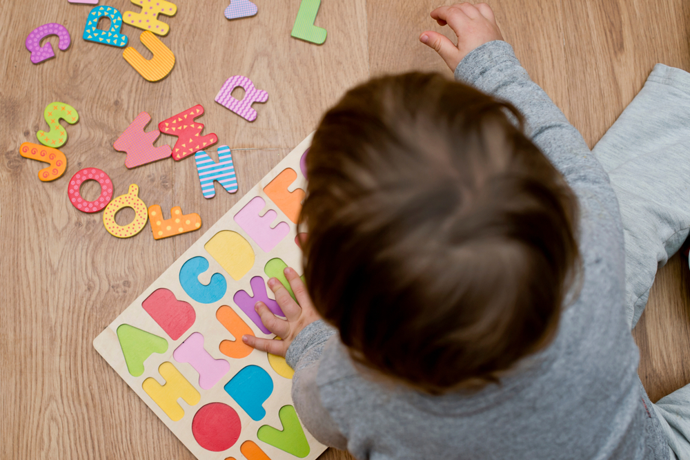 Bambino seduto sul pavimento che gioca con numeri e lettere in legno