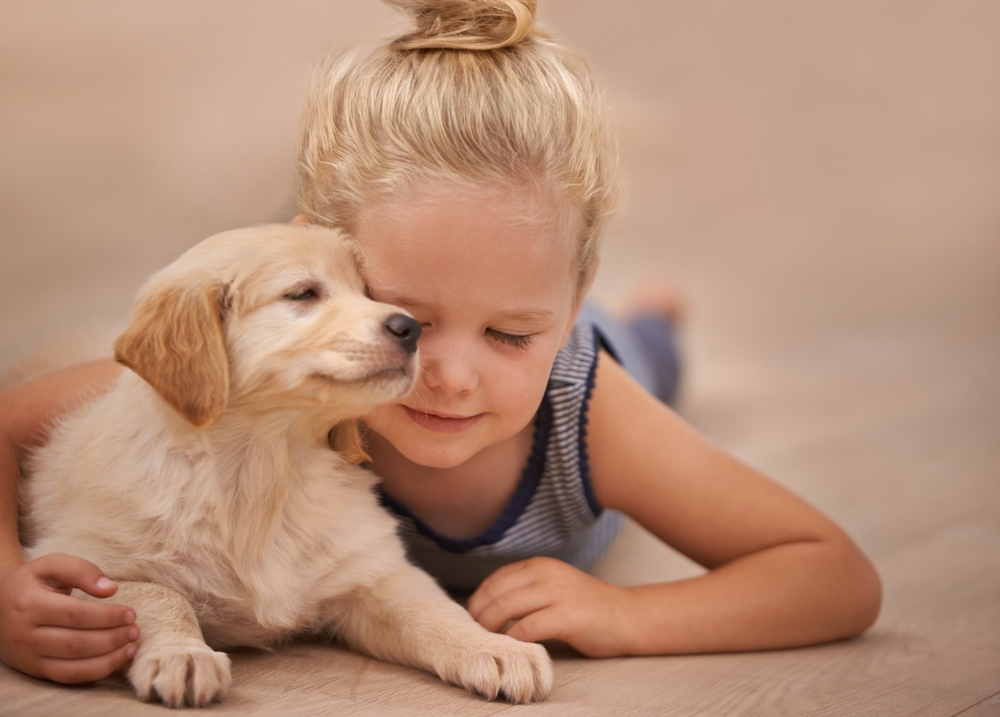 Bambina sdraiata sul pavimento che abbraccia affettuosamente il suo cagnolino