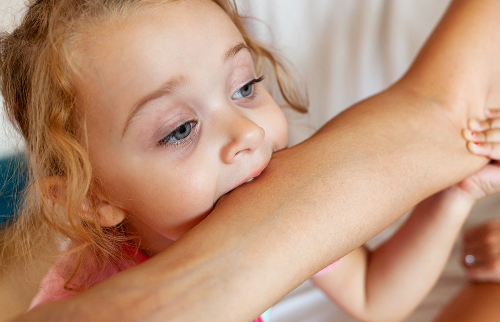 Bambina che morde il braccio della mamma