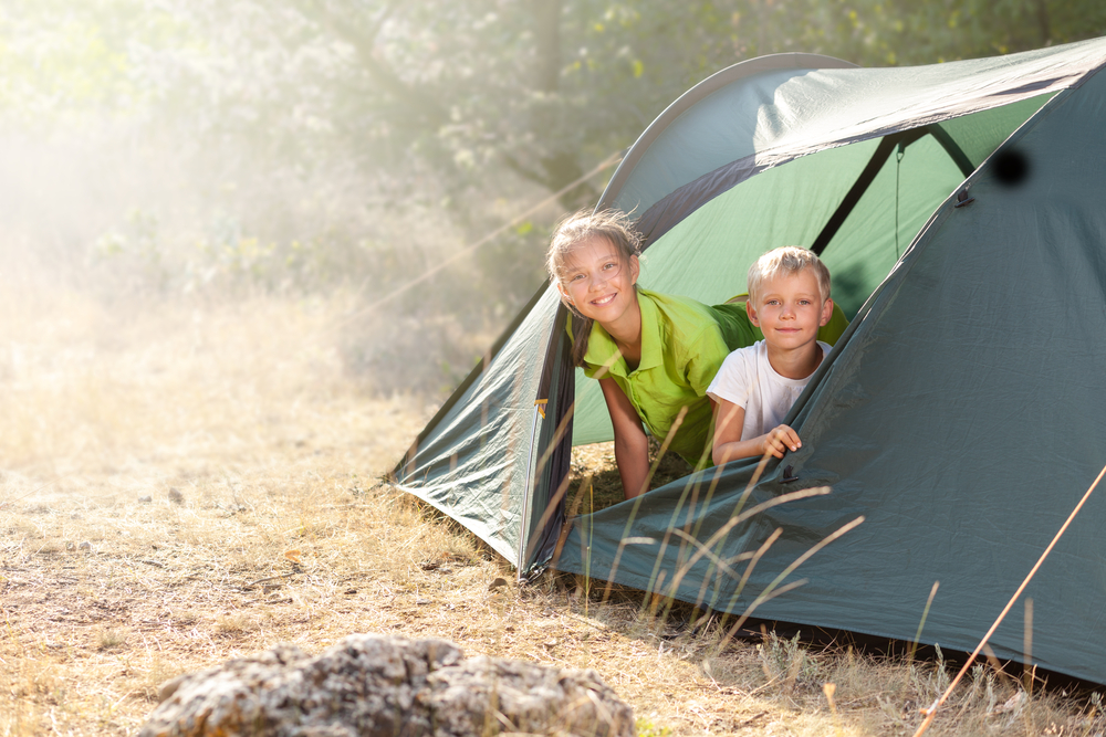 Bambini sorridenti in campeggio dentro una tenda