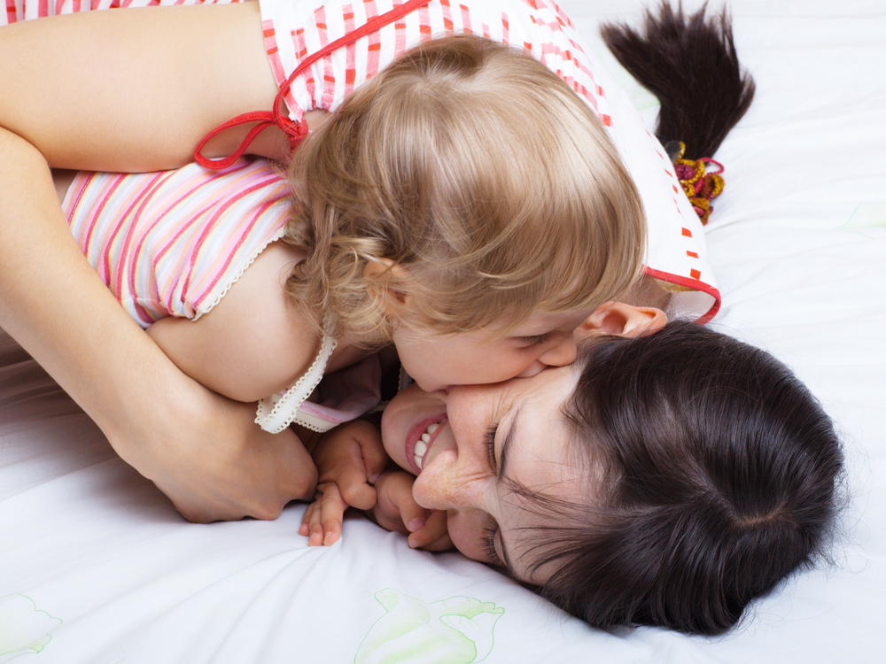 Bambina che morde la mamma mentre gioca sul letto