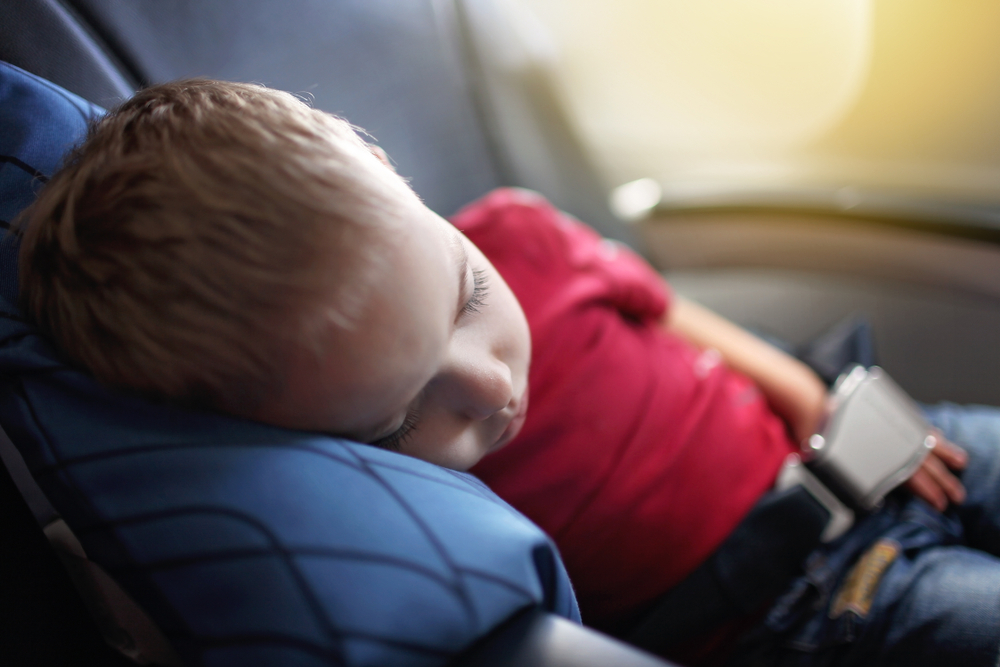 Bambino che dorme con la testa sul cuscino durante il volo in aereo