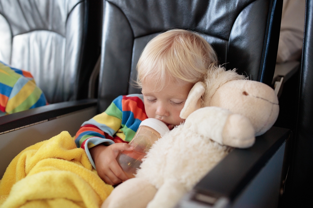 Bambino in aereo durante il volo che dorme con biberon, peluche e coperta