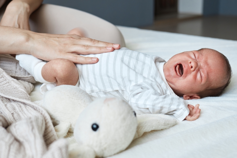 Madre che massaggia il pancino del suo bambino mentre sta piangendo per una colica