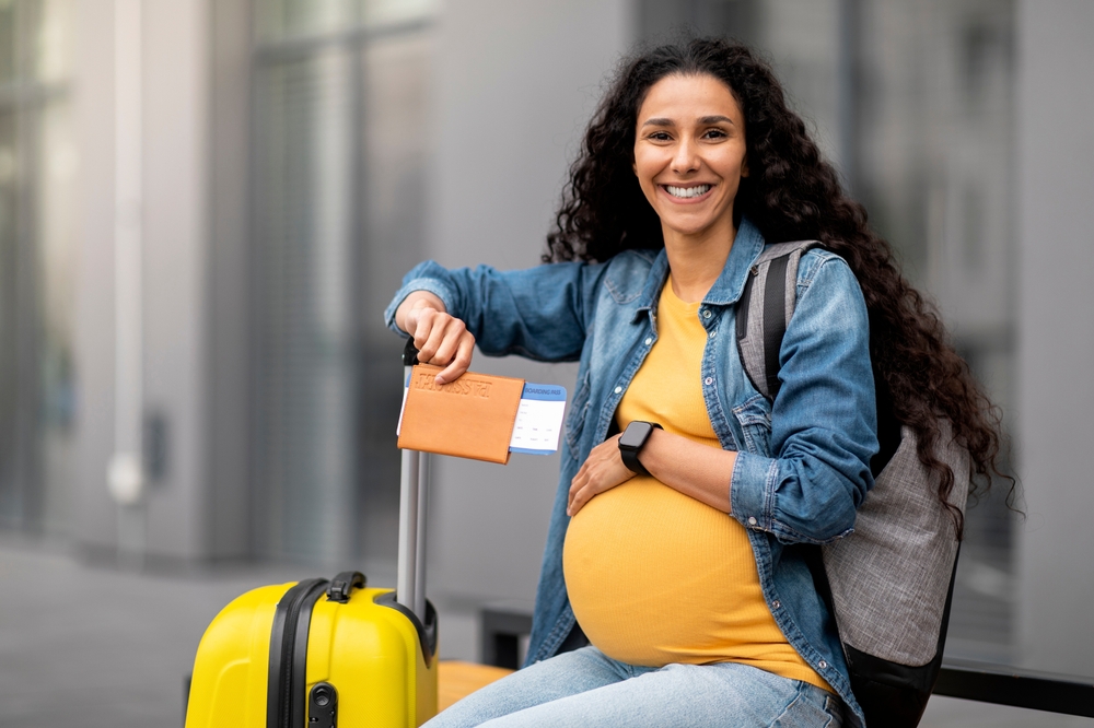 Donna incinta con zaino e valigia in aeroporto, con in mano passaporto e biglietti