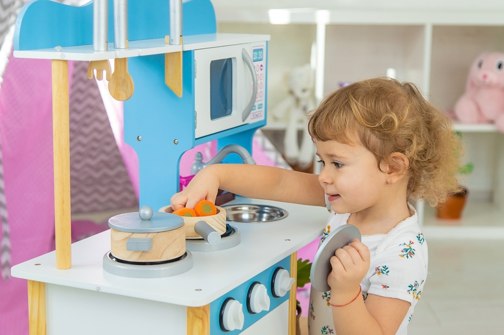 Bambina che gioca con cucina, piatti e alimenti di legno