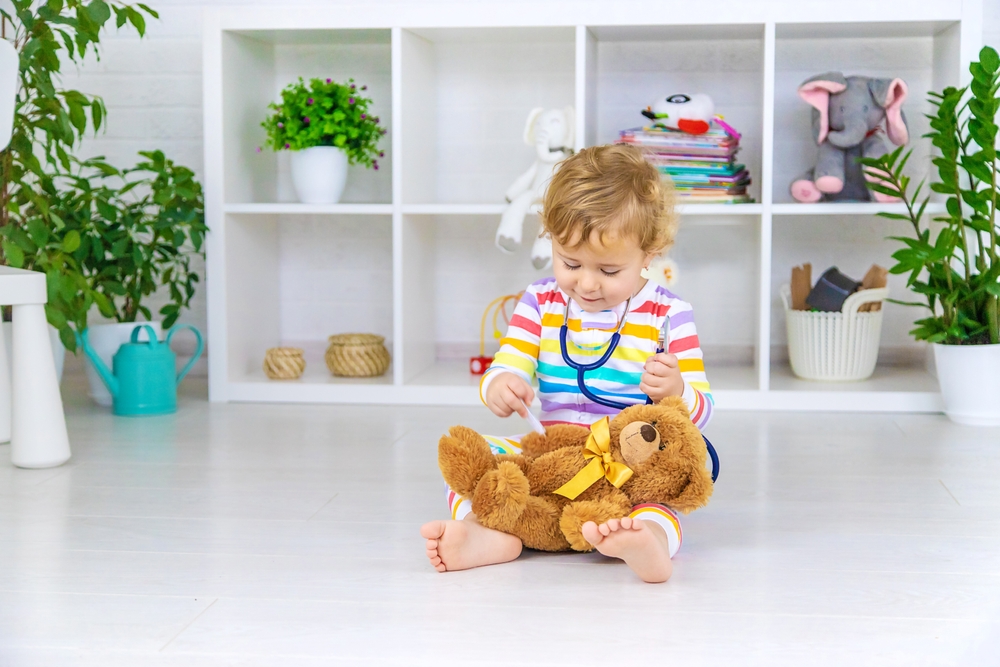 Bambino che imita il dottore con il kit del medico in plastica e un pupazzo come paziente