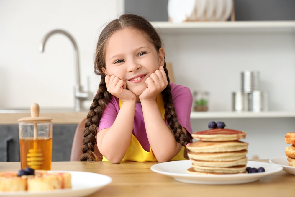 Bambina sorridente in cucina con piatto di pancake con frutta fresca da gustare a colazione