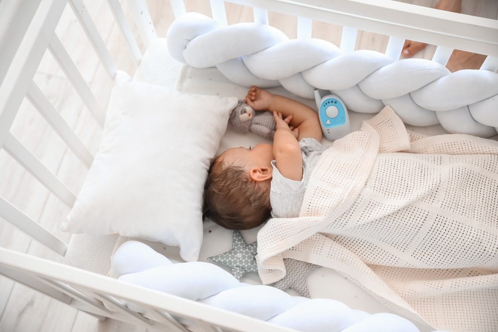 Neonato che dorme nella culla accanto a un giocattolo e a un baby monitor