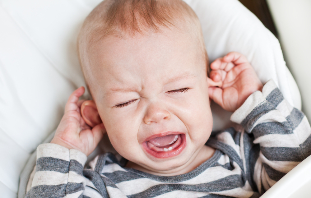 Neonato con dolore da otite che piange toccandosi le orecchie