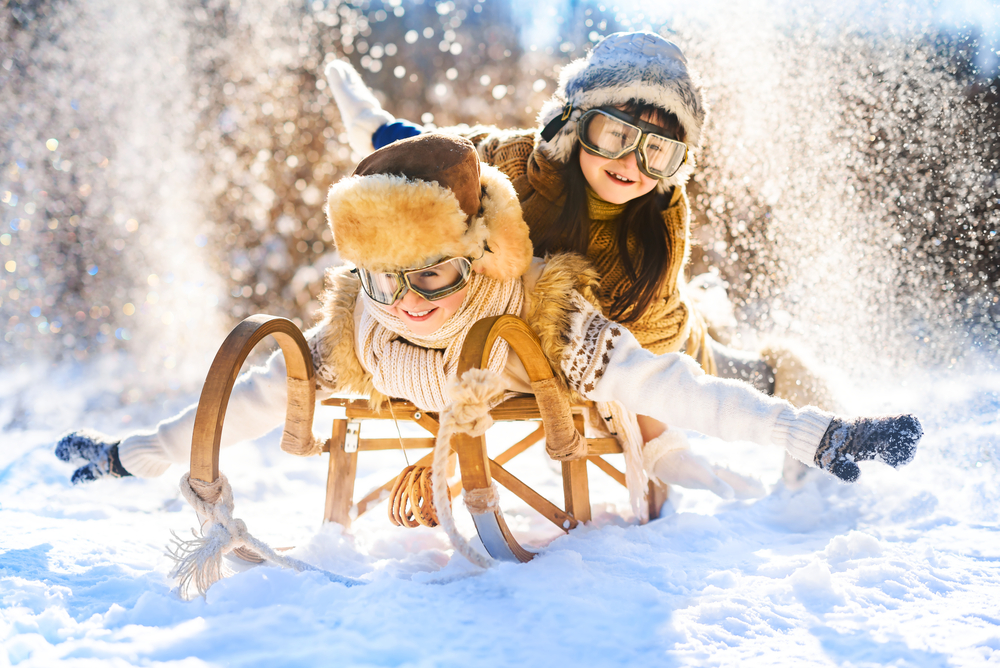 Due bambini sorridenti giocano sulla neve con uno slittino di legno in montagna