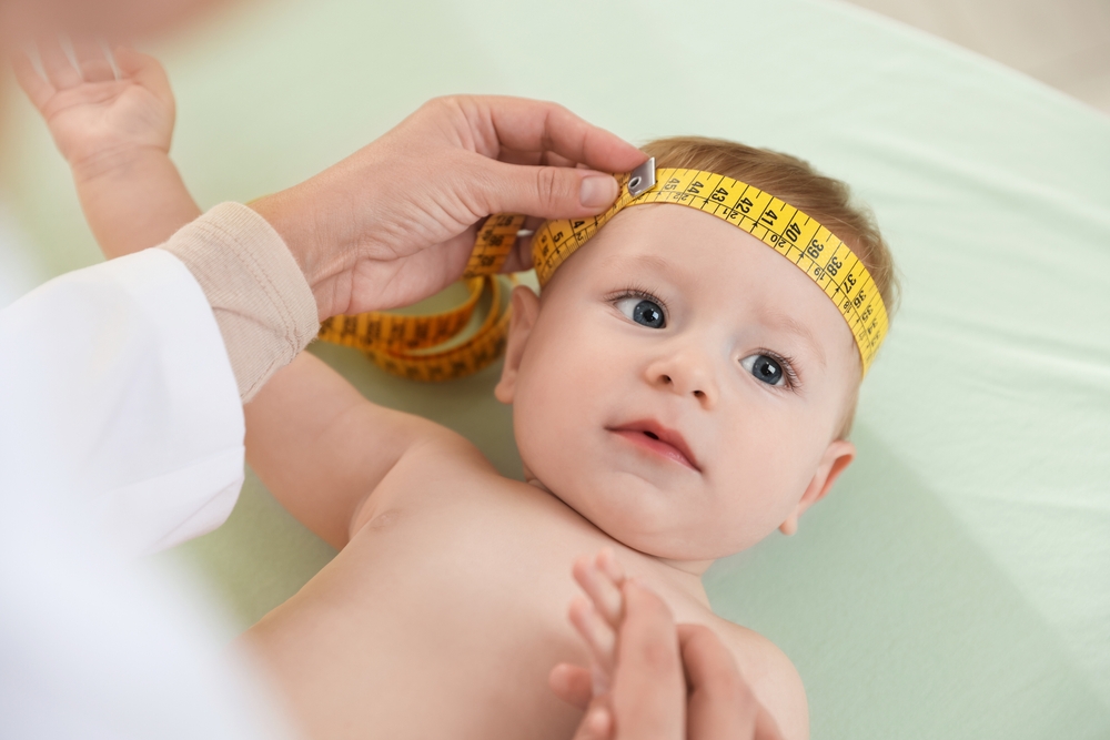 Pediatra che misura la circonferenza cranica del neonato con un metro da sarta