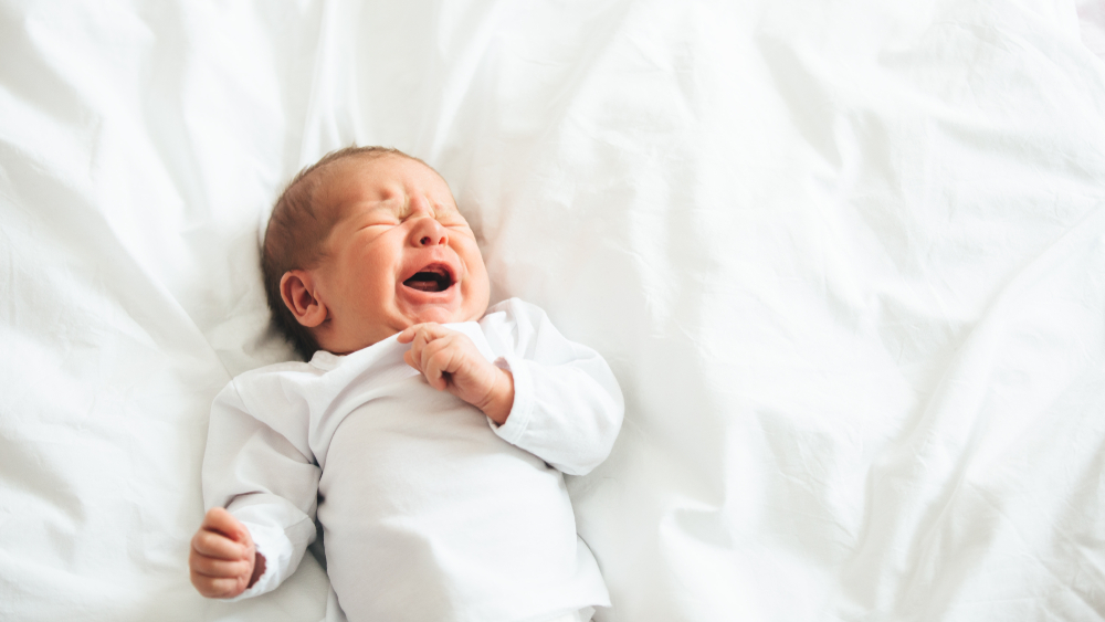 Neonato che piange sdraiato sul letto con lenzuola bianche