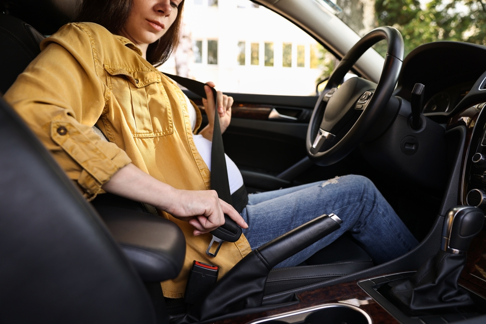 Donna incinta seduta in auto che allaccia la cintura di sicurezza