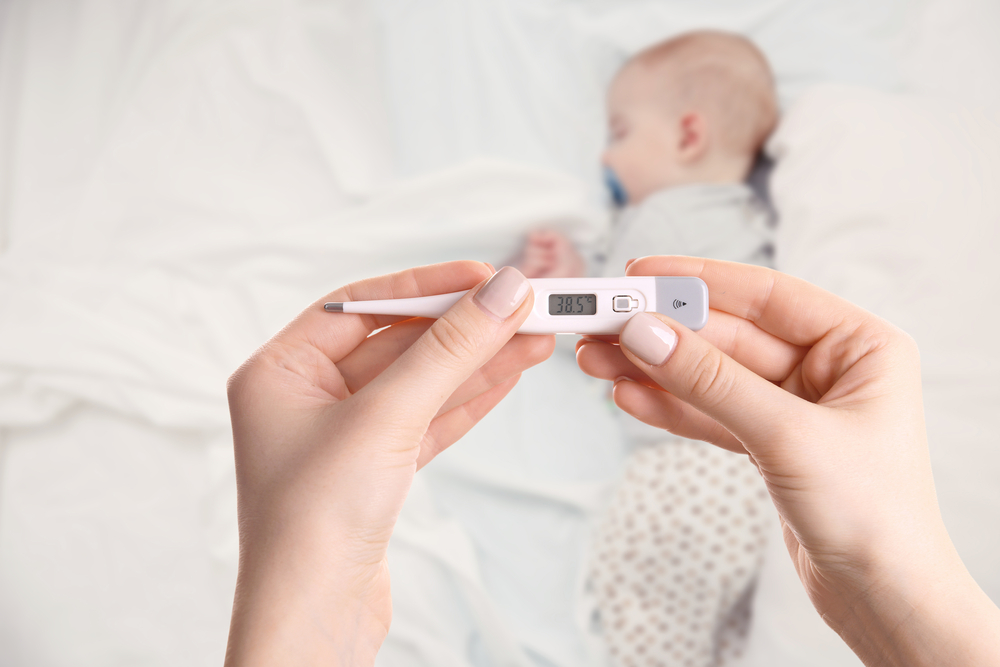 Primo piano di mani che tengono un termometro digitale e sullo sfondo un neonato che dorme nel letto