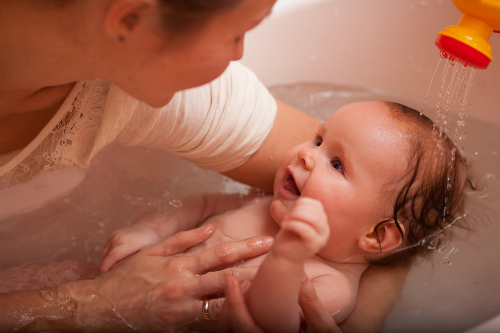 Bambino sorridente durante il bagnetto serale, tenuto tra le braccia della madre