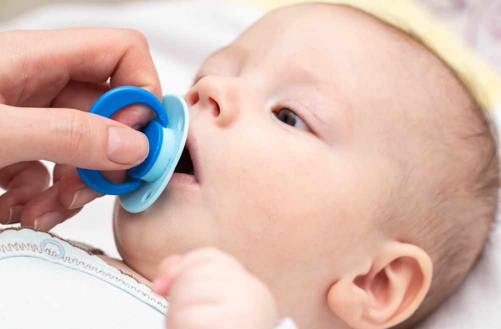 Mano della madre che avvicina un ciuccio azzurro alla bocca del neonato sdraiato