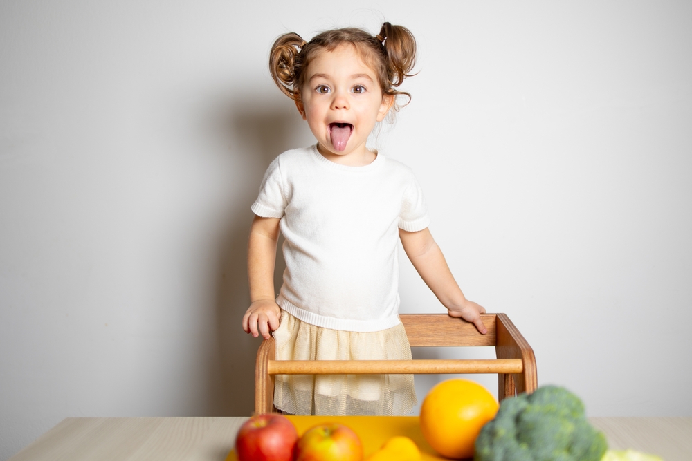 Bambina divertita sulla torre montessoriana davanti a un tavolo con frutta e verdura