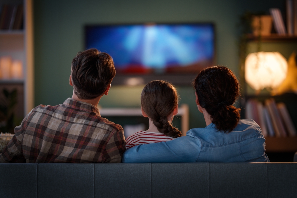 Famiglia seduta sul divano di spalle mentre guarda un film alla televisione