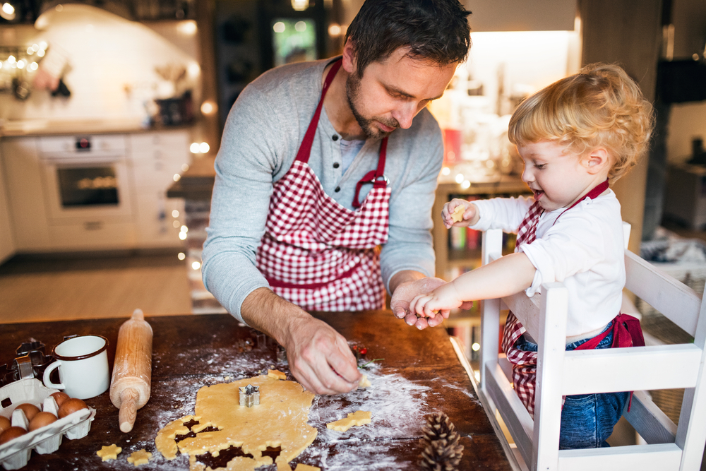 Bambino su torre montessoriana che aiuta il padre a preparare i biscotti in cucina