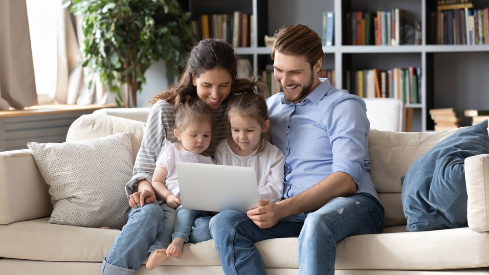 Famiglia con due bambine piccole seduta sul divano che guarda insieme un laptop in salotto